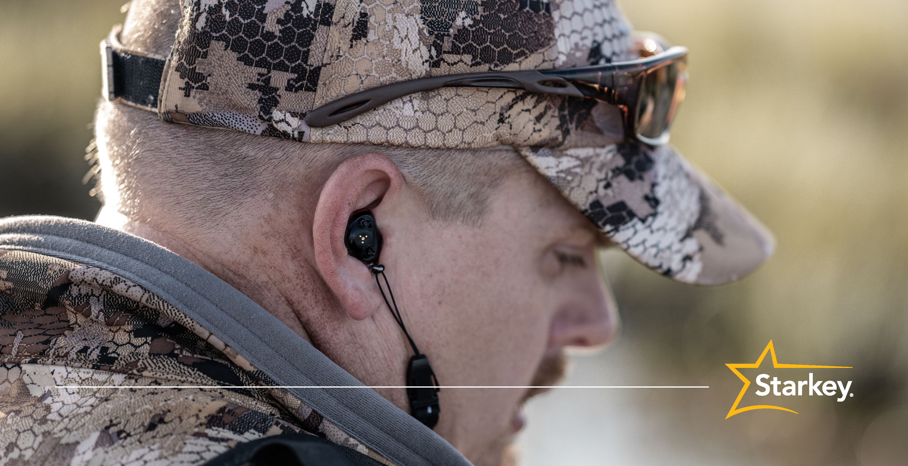 Close up of man wearing brown camouflage clothing and SoundGear Phantom hearing protection in right ear 